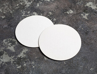 Two blank beer coasters on concrete surface.