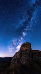 A striking night sky panorama showcasing the Milky Way above large, moss-covered boulders.