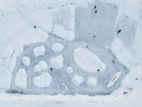 Aerial view of a frozen lake surface fractured into icy mosaics, contrasting stark white snow with translucent ice, reflecting the winter sky, Vilnius, Vilnius County, Lithuania.