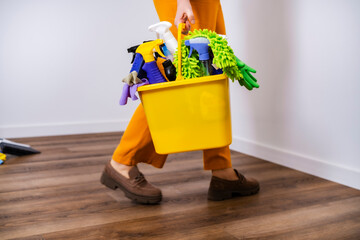 Housewife walks with yellow bucket full. Professional woman in orange trousers does housework....