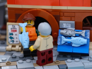 Obraz premium Tambov, Russian Federation - January 19, 2026 Lego fisherman minifigure selling a light blue fish from a fish stall to a customer on a city street.