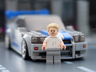 Obraz premium Tambov, Russian Federation - August 21, 2025 Lego Brian O'Conner minifigure standing in front of his Nissan Skyline GT-R (R34) car in city street. 2 Fast 2 Furious movie. Lego Speed Champions.