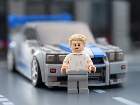 Tambov, Russian Federation - August 21, 2025 Lego Brian O'Conner minifigure standing in front of his Nissan Skyline GT-R (R34) car in city street. 2 Fast 2 Furious movie. Lego Speed Champions.