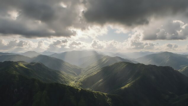 Sunlight breaks through clouds over a range of green, rolling mountains