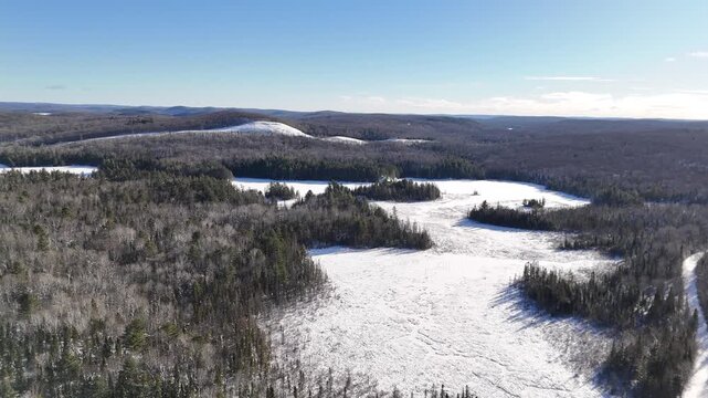 Bright, sunny aerial view of a snowy forest surrounding two partially frozen Oram Lake in Algonquin Provincial Park