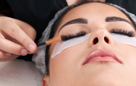 Cosmetologist making eyelash extention and correction using brush