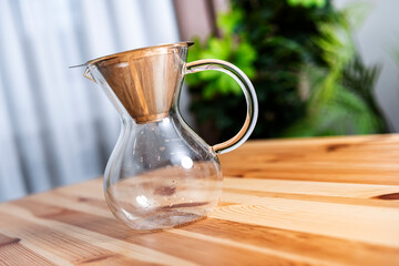 Glass coffee decanter with metal filter on wooden desk. Alternative pour over brewer equipment in kitchen. Lifestyle, hobby, morning, craft and barista concept