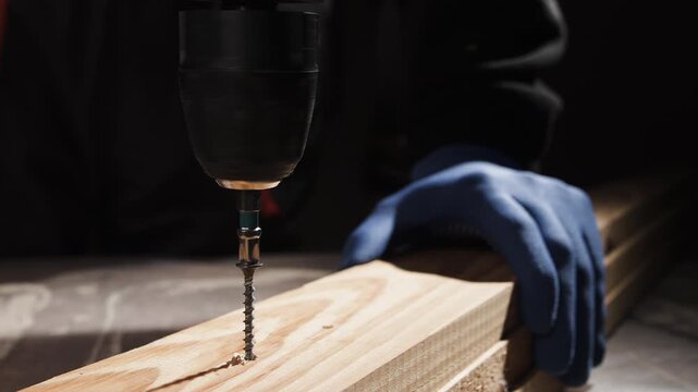 Close up of carpenter hand unscrewing screw from wood with cordless drill.