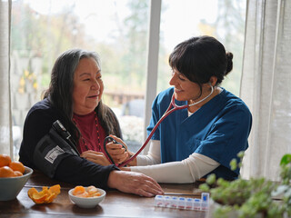 Native American nurse with stethoscope taking patient's blood pressure at home