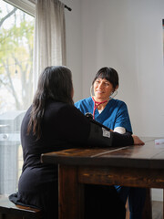 Native American nurse and elderly patient sit at table to check blood pressure