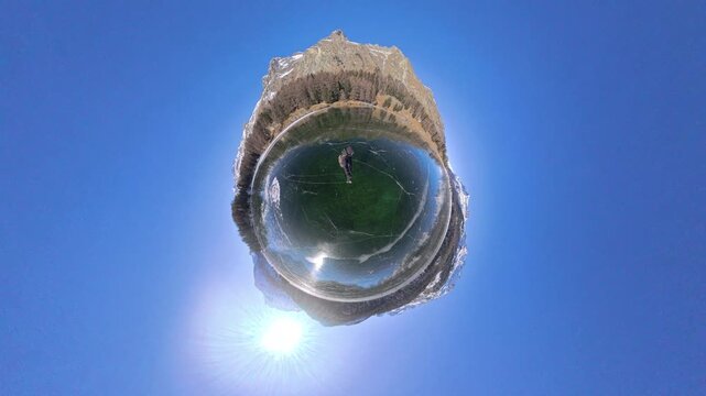 Tiny planet view of a man skating across crystal-clear alpine ice on Lake Sils