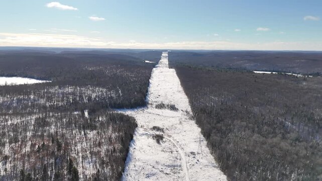 Aerial view moving along the cleared New Algonquin Provincial Park transmission line corridor through a snow-covered wilderness area in Ontario, Canada
