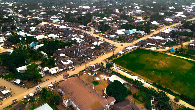 Aerial view of rooftops blending with the earth tones, punctuated by verdant fields and the intricate crisscross of roads, Oduoha-Emuoha, Rivers, Nigeria.