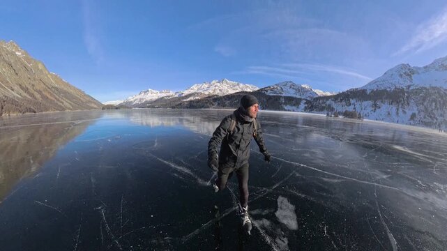 Man ice skating across mirror-like frozen Lake Sils with mountain reflections, Switzerland