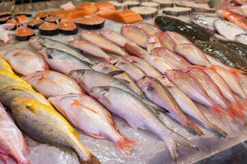 Fototapeta premium A vibrant assortment of fresh whole fish and thick salmon steaks is meticulously arranged on a bed of crushed ice at a bustling wet market in Hong Kong.