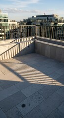 Naklejka premium Modern rooftop terrace floor receives strong shadow patterns from a surrounding metal railing structure