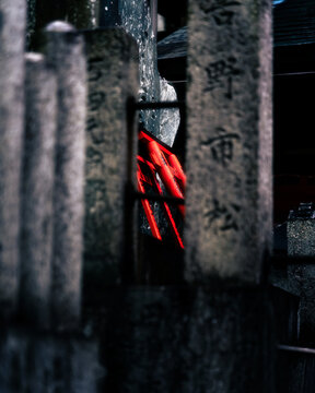 Kyoto, Japan - 18 January 2026: View of ancient stone markers stand guard, framing a glimpse of vibrant red architecture within a shadowy temple precinct.