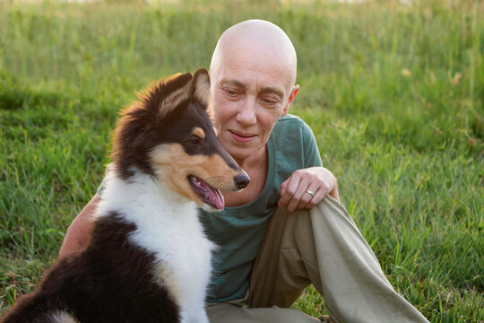 Elderly woman with alopecia due to chemotherapy treatment with a collie puppy. Concept of alternative and emotional therapy for cancer patients