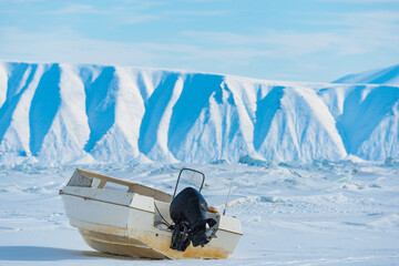 Boat on frozen sea near Qaanaaq village in Greenland during winter with ice mountains in the background © Mikael