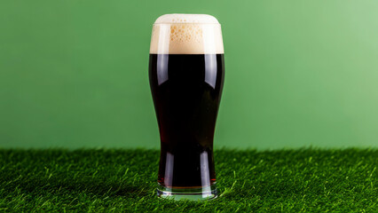 Dark stout beer glass with frothy head on green grass and simple background