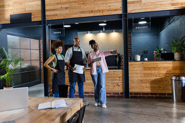 African American staff in dark aprons planning service at counter, holding tablet and papers