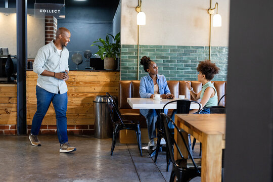 African friends chatting and drinking coffee at cafe booth with white square table, COLLECT sign