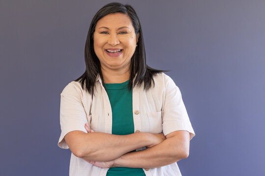 Woman standing with arms crossed, smiling broadly while wearing green top and beige button shirt