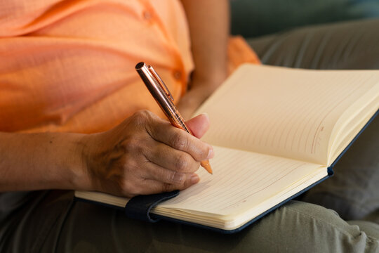 Metallic pen is hovering above lined notebook resting on lap near cushion, with warm lighting