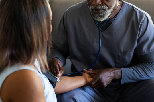 African American male provider in gray scrubs examining patient in clinic with stethoscope and cuff