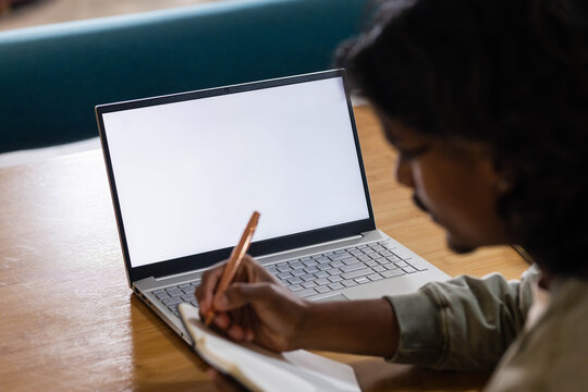 Open laptop is glowing with blank white screen on wooden table, notebook and pen resting