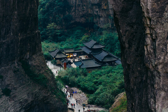 Aerial view of an ancient temple nestled amidst the verdant foliage, framed by towering cliffs, a testament to time and nature's embrace, Wulong, Chongqing, China.