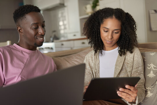 Young multiracial couple smiling while using a tablet and laptop at home