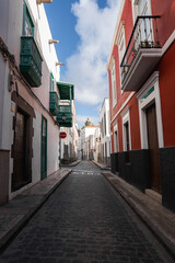 Whitewashed and terracotta buildings lead to a church dome in Las Palmas. Green wooden balconies and a no entry sign mark a one way alley under soft daylight. © Aerial Film Studio