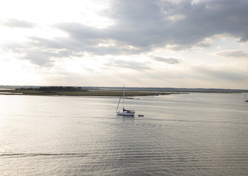 Aerial view of a lone sailboat glides across the tranquil water, reflecting the soft, diffused light beneath a vast, textured sky, Fernandina Beach, Florida, United States.