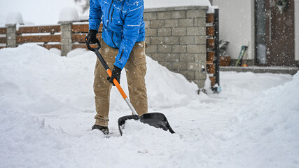 Man clearing snow from a driveway using a snow shovel. Winter sidewalks maintenance. © Sabrewolf