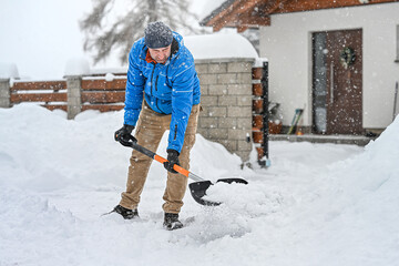 Man clearing snow from a driveway using a snow shovel. Winter sidewalks maintenance. © Sabrewolf