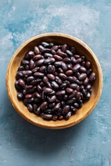 Fototapeta premium Wooden bowl of raw black beans on textured blue surface