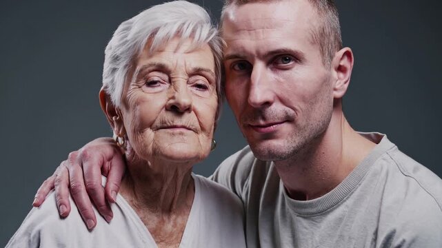 Handsome young man warmly hugging his elderly grandmother, both gazing at the camera with emotions shifting from solemn to joyful