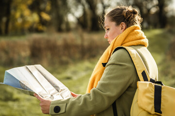 Woman with backpack  holds a paper map in a forest.
