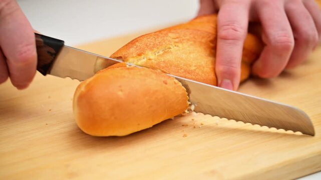 A person is cutting a loaf of bread on a wooden cutting board. The bread is sliced into pieces, and the knife is being used to cut it. Concept of simplicity and routine