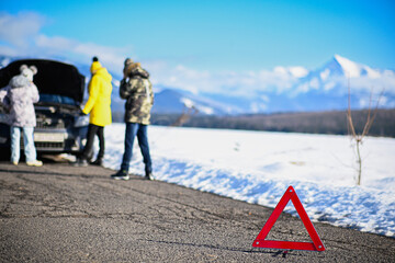 Red warning triangle on road signaling car trouble for family traveling in winter