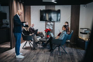 Professionals gather in a modern office lounge for a casual business meeting. Laptops and tablets are in use as a presenter speaks, with Christmas stockings and poinsettia adding festive decor.