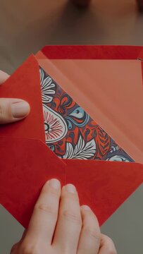 Vertical video: Peeling right hand pulling flap on red envelope in warm room, checking floral liner