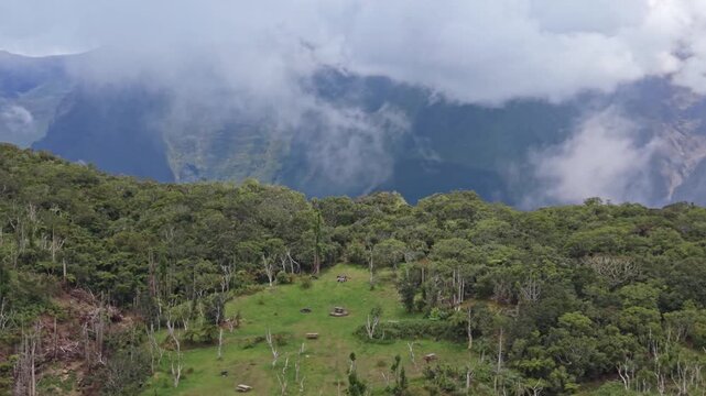 Drone orbit shot over picnic clearing surrounded by lush tropical forest, slowly moving forward to reveal dense vegetation and mountain slopes under low clouds, Sentier Botanique Notre-Dame de la Paix