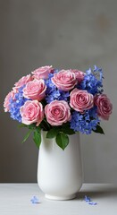 Fototapeta premium A vibrant arrangement featuring soft pink roses mixed with delicate blue blooms, presented beautifully in a clean white ceramic vase on a surface, vase, stem, blossom