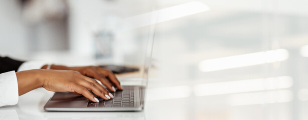 Two hands are seen typing on a laptop at a bright workspace. The setting highlights focused work...