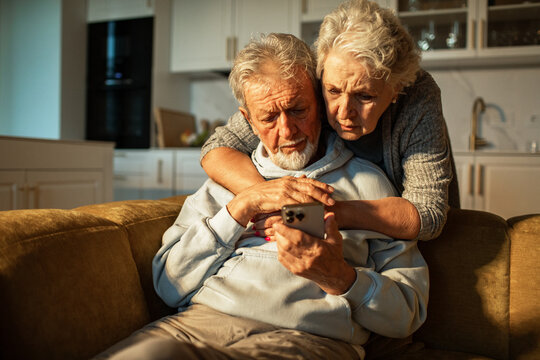 Concerned senior couple looking at smartphone at home