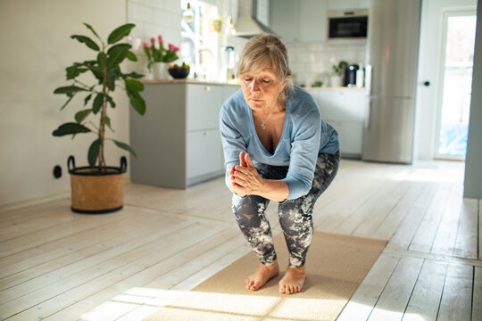 Senior woman practicing yoga balance in home kitchen