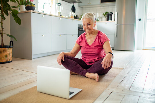 Senior woman following online yoga class in home kitchen