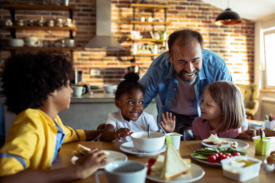 Smiling father with children having breakfast in home kitchen